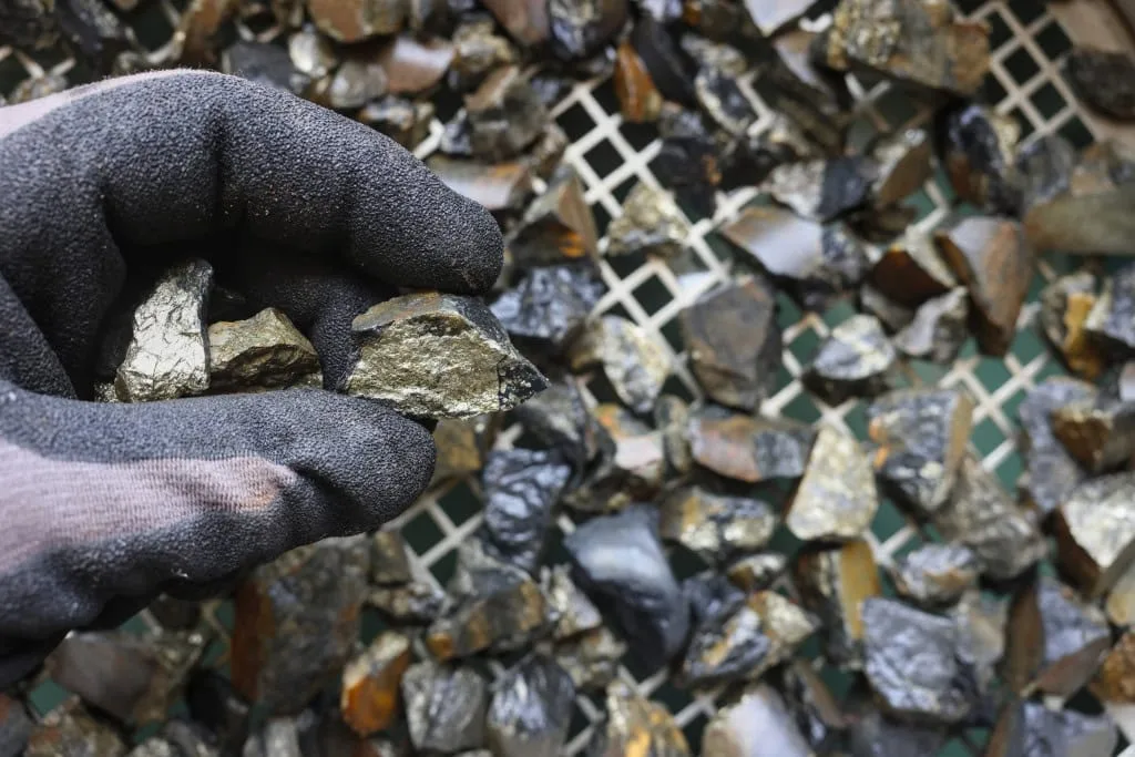 Close-up de minerais brilhantes, simbolizando recursos tecnológicos e a exploração consciente, com um fundo desfocado de componentes eletrônicos
