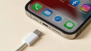 Smartphone iPhone sendo conectado a um carregador com cabo USB-C, mostrando o ícone de bateria carregando na tela.