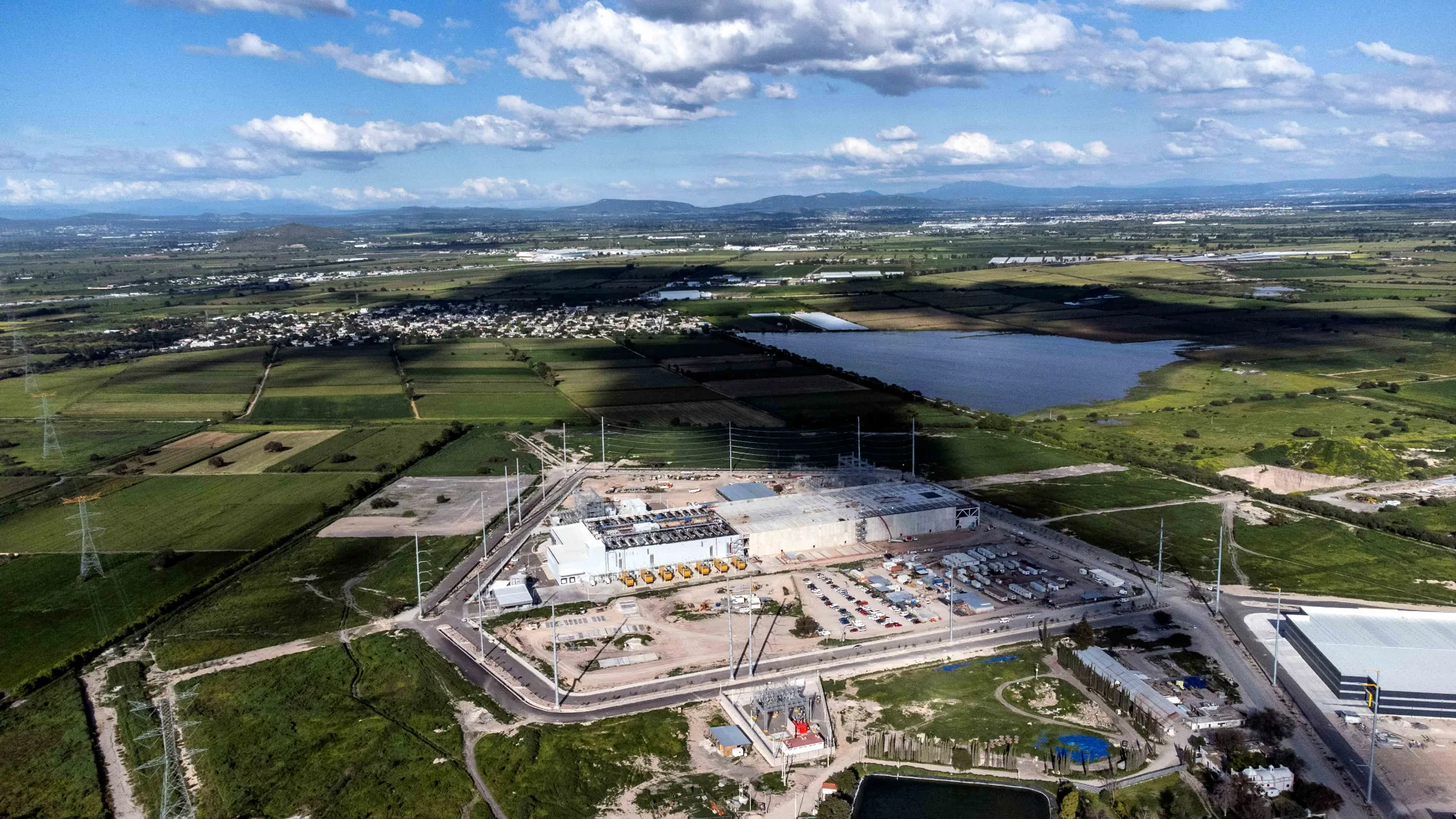 Visão aérea de um data center moderno com turbinas eólicas e painéis solares ao fundo, simbolizando a busca por energia sustentável para a IA.