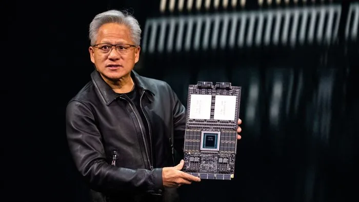 Jensen Huang, CEO da NVIDIA, sorrindo e gesticulando, com um fundo verde que remete à identidade visual da empresa. A imagem capta um momento de discussão sobre tecnologia e negócios.