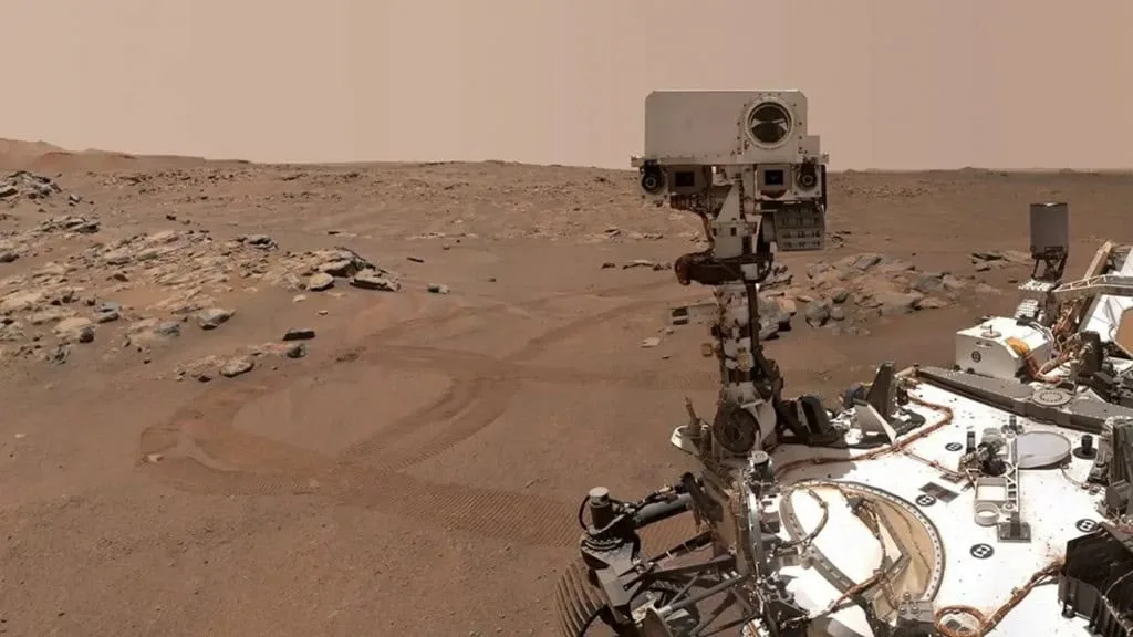 Imagem do rover Perseverance da NASA fotografando a superfície rochosa de Marte, sob um céu avermelhado.