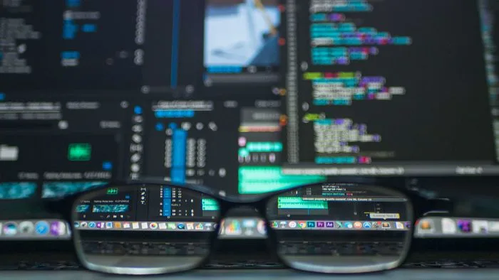 Mão digitando em um notebook com códigos de programação na tela, simbolizando a área de TI.