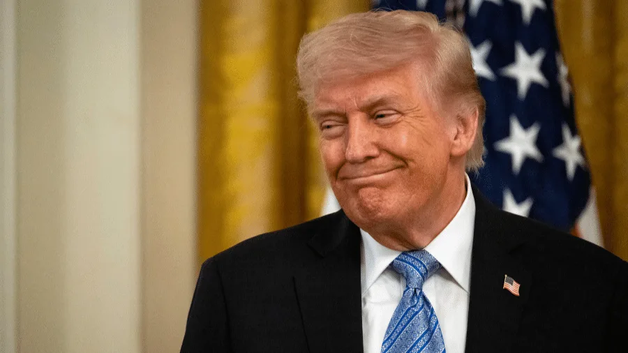 Donald Trump gesticulando em um pódio, com bandeiras americanas no fundo, simbolizando a postura do governo dos EUA em relação à regulamentação da IA.