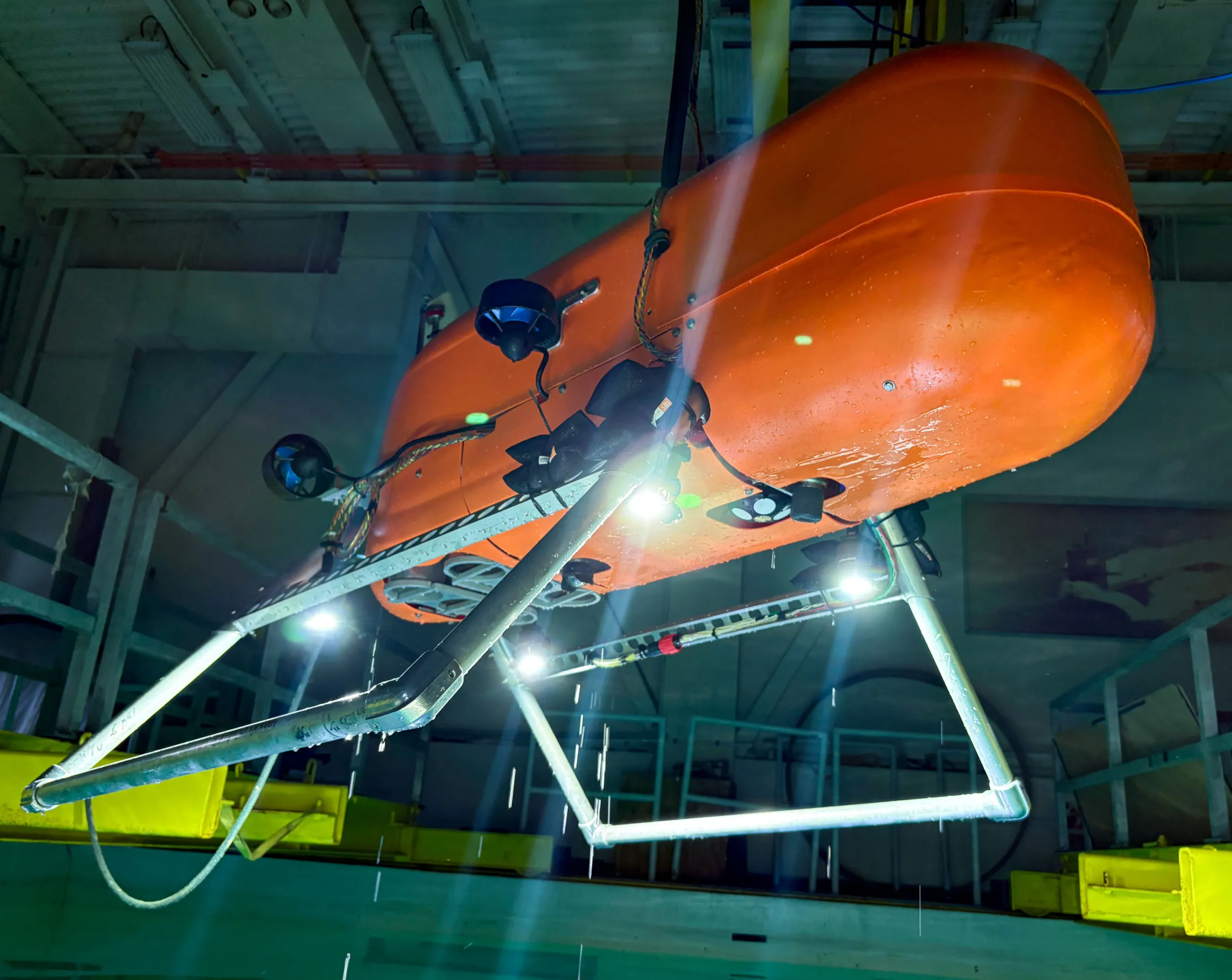 Dois submersíveis robóticos alaranjados e neon do Orpheus Ocean flutuam em um fundo escuro, com contornos azuis e amarelos, destacando seu design compacto e inovador.